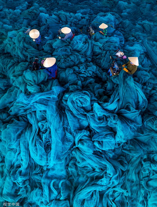 越南工人缝补巨型渔网 好似置身深邃蓝色海洋 